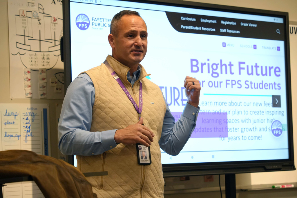 A man in a yellow vest and blue shirt stands before a screen displaying "Bright Future" in a classroom.