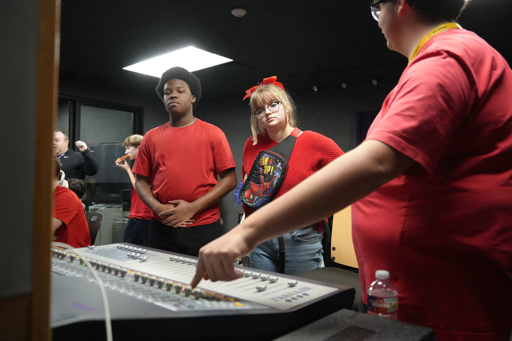 A group of people in red shirts working on a sound mixing board in a room.
