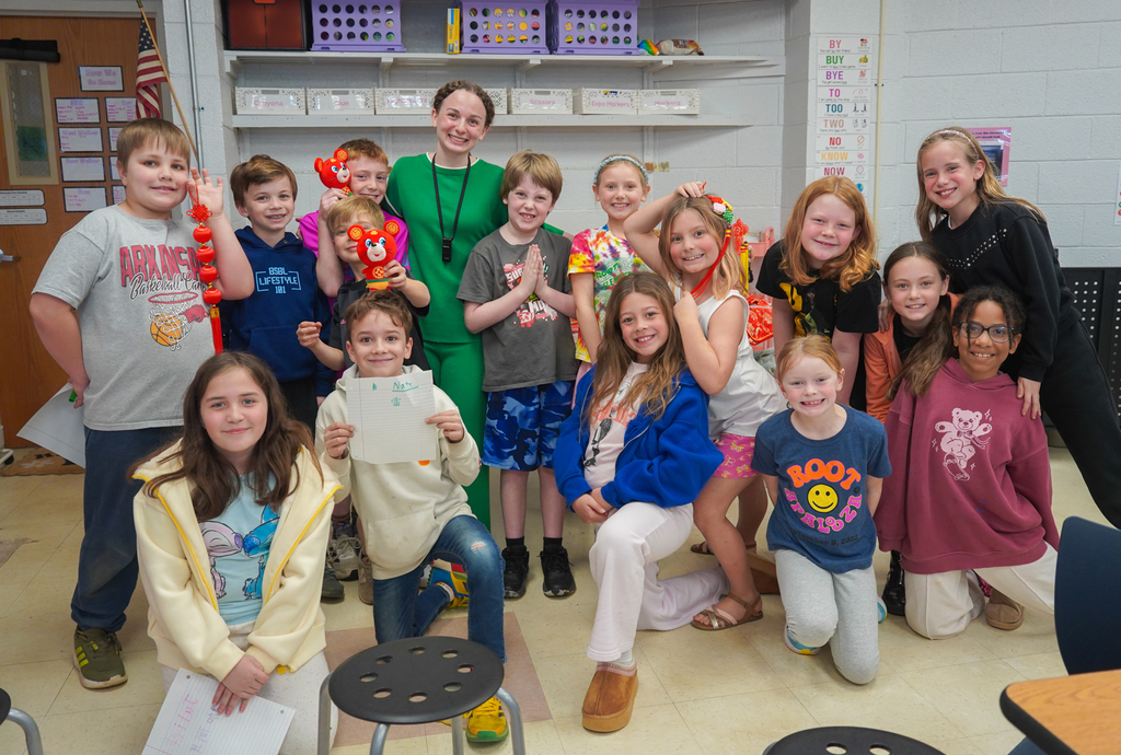 Kids and a teacher posing for a picture with crafts in a classroom with shelves.