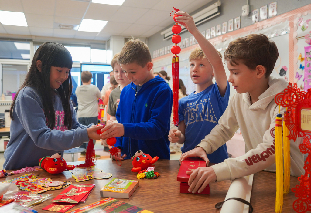Four children at a table, crafting red paper decorations with red objects, surrounded by colorful paper.