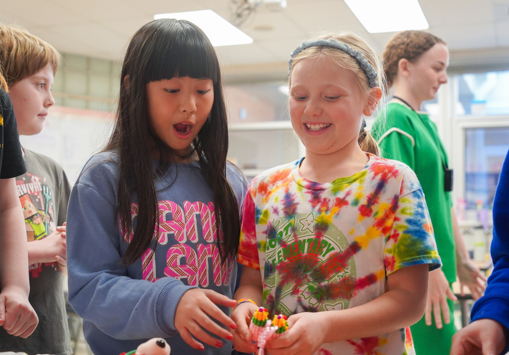 Two girls in a classroom, one with a tie-dye shirt and another in a blue sweatshirt.