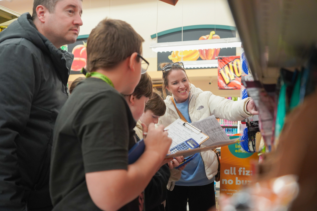 A woman points to a shelf as a man and three children look on. Shelves with items are in the background.