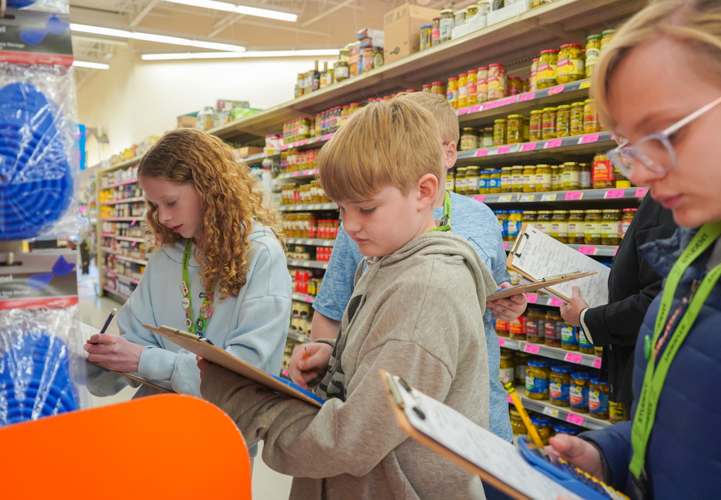 Several children with clipboards in a store, standing near shelves with colorful products.