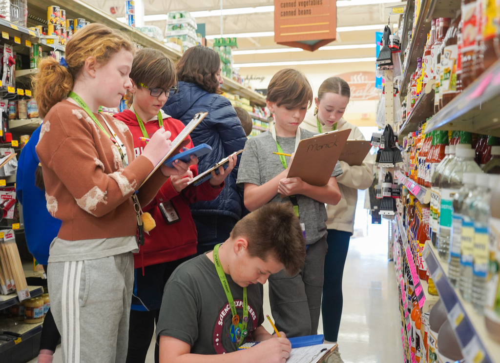 Five young people in a store aisle, looking at items on the shelves and taking notes.