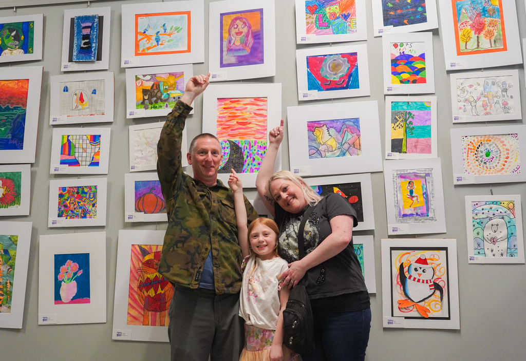A man, a woman, and a child stand before a wall with colorful artwork.