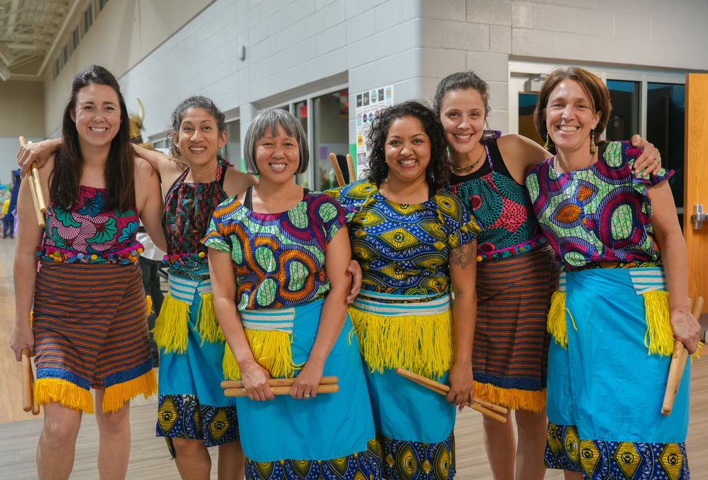 A group of women dressed in vibrant traditional attire, possibly for a cultural event, stand together in a room.