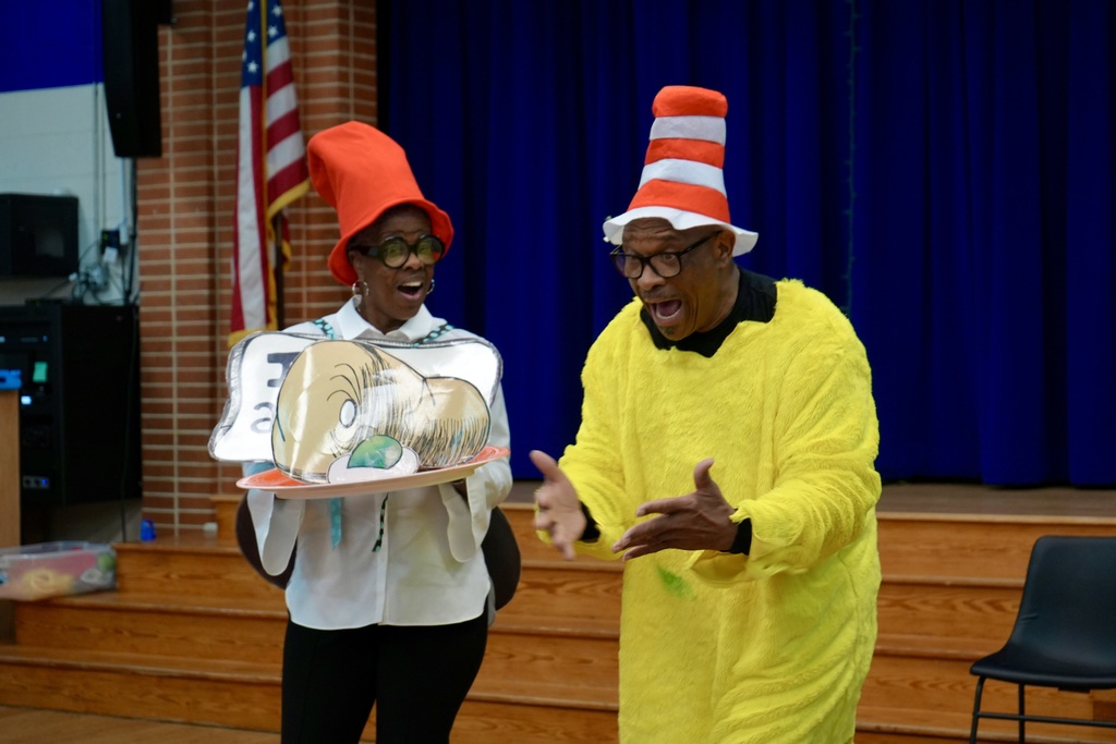Two people dressed in costumes, one in a white shirt and one in a yellow suit, on a stage.