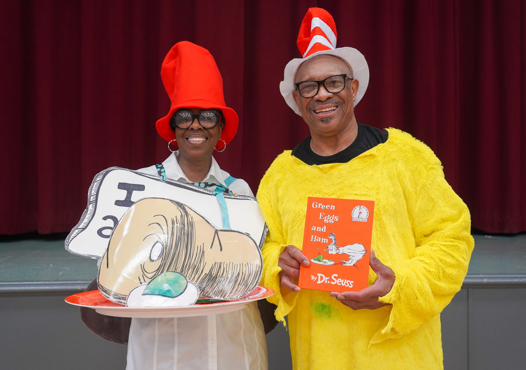 Two people dressed as Cat in the Hat and Thing 1 hold props and books in a theater.