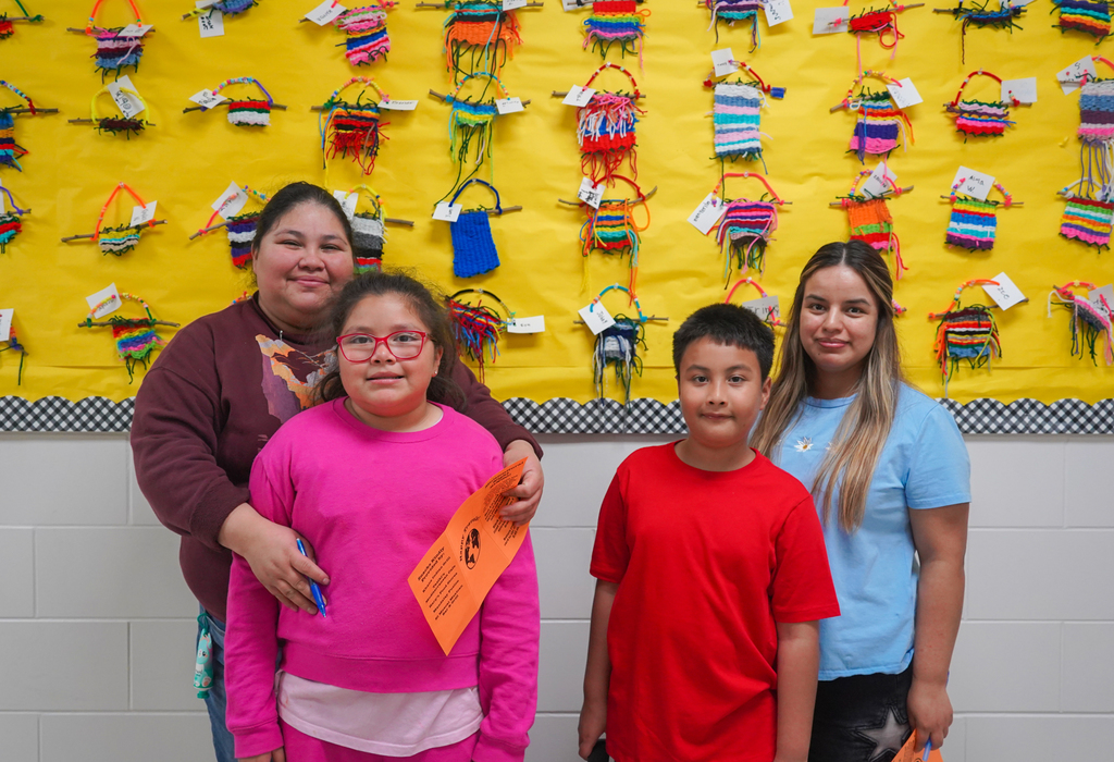 Three children and an adult woman pose for a photo in front of a bulletin board.