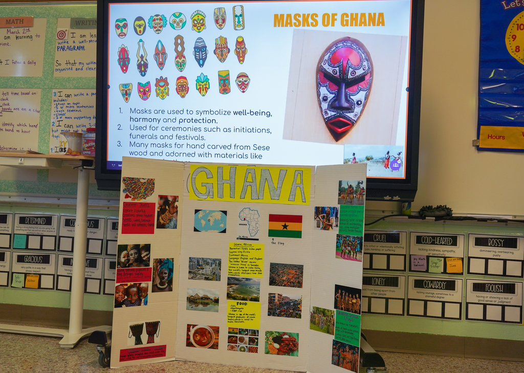 A classroom with a large screen showing "Masks of Ghana" and a display board with photos and information.