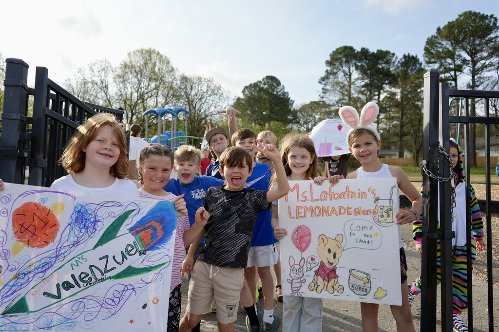 A group of children holding signs with drawings and text, standing in front of a black gate.