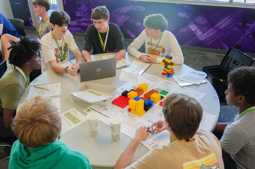A group of students sit around a table with laptops, papers, and a colorful object.