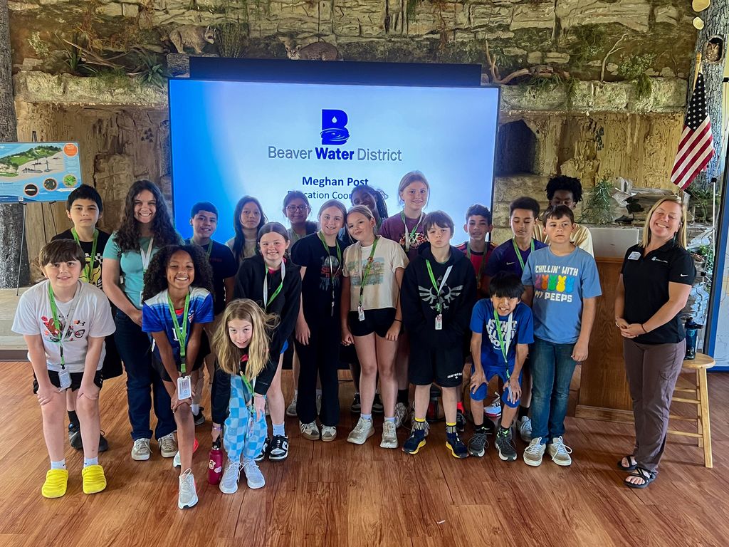 A group of children and an adult pose for a photo in a room with a large projector screen.