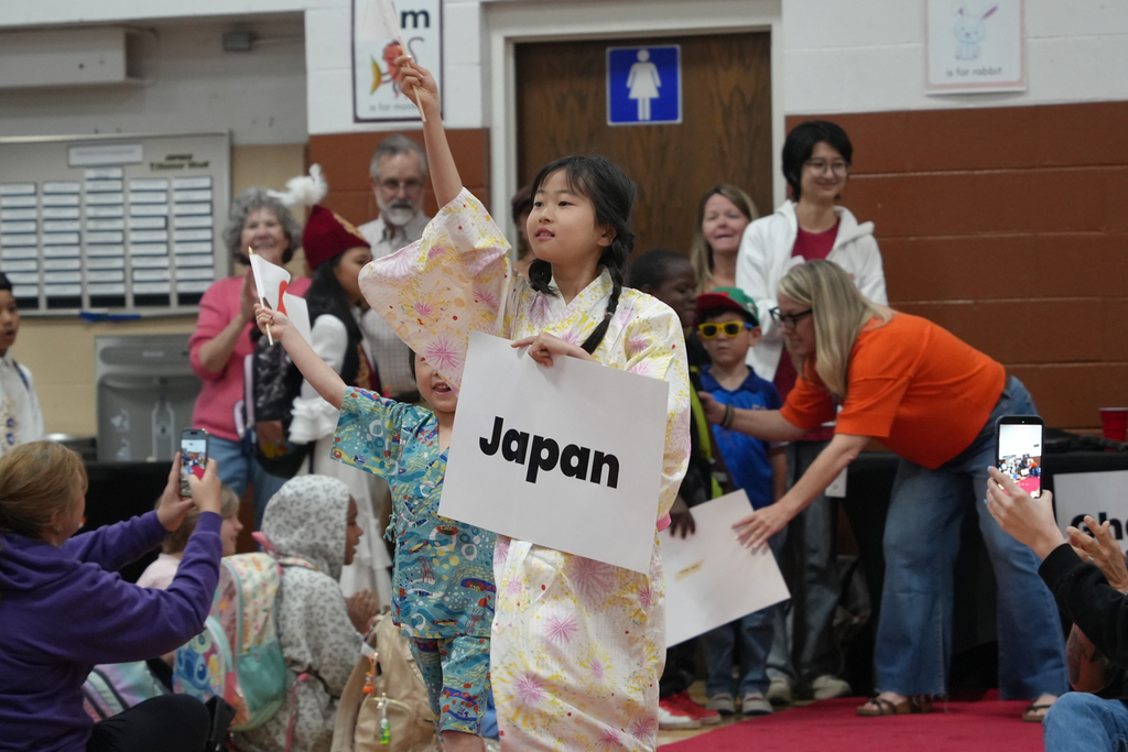 A girl in a kimono holding a sign reading "Japan" while others in traditional attire stand behind.