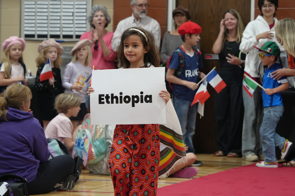 A young girl stands in a group, holding a sign that reads Ethiopia. Various people, including children, are in the background.