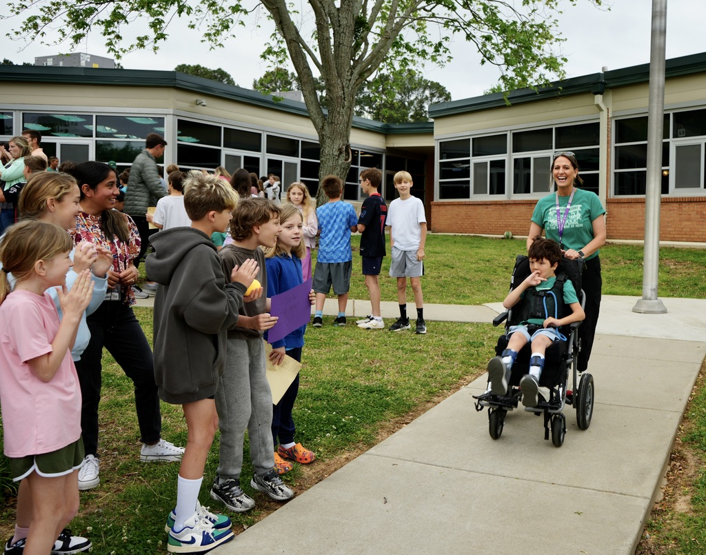 A group of children in a courtyard, a woman in a green shirt pushing a child in a wheelchair.