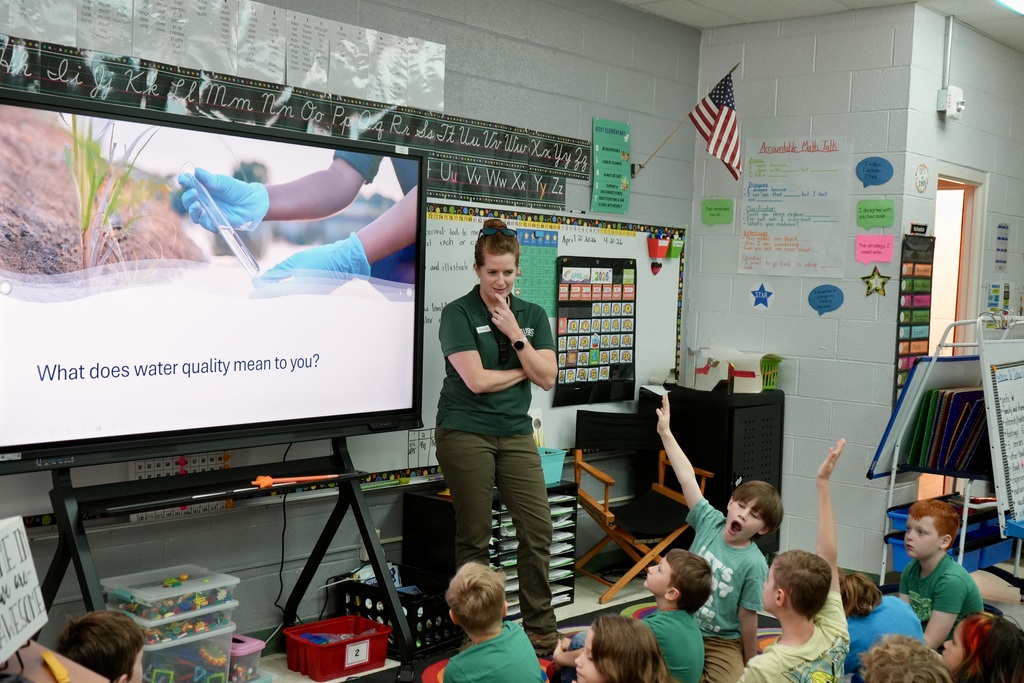 A teacher presents a screen showing an image of a plant to a classroom of students.