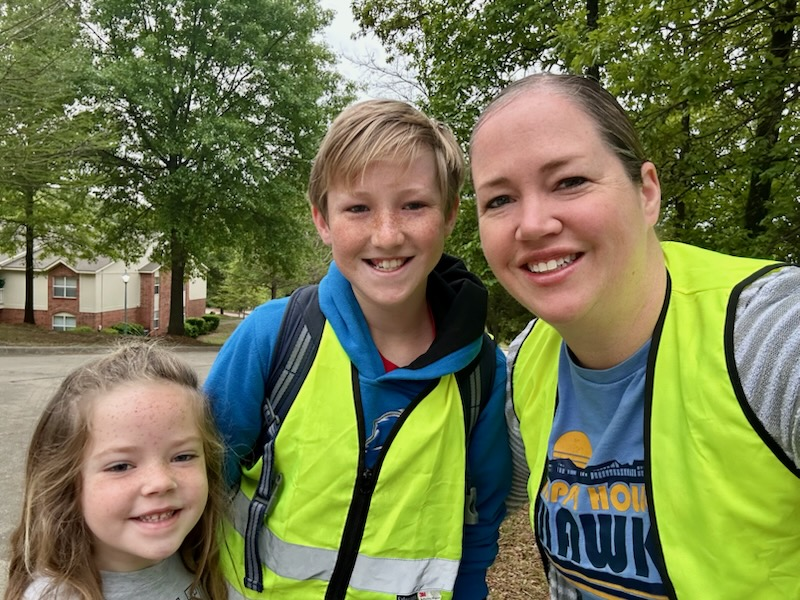 Two women and a boy stand outside, smiling. Trees and buildings are in the background.