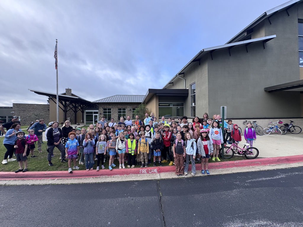 A group of children, adults, and bicycles on the sidewalk in front of a building.