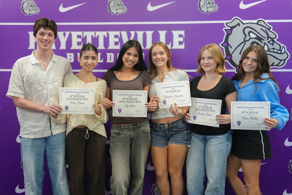 Six individuals stand in a row, holding certificates. Behind them is a purple backdrop with text and a logo.