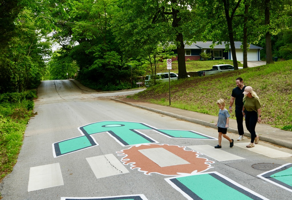 Family walks on a pedestrian crossing painted with a green turtle design in a neighborhood.