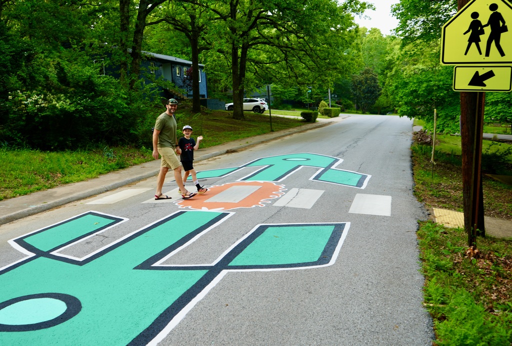 Two people walk across a crosswalk on a street. The crosswalk is painted in blue and green shapes.