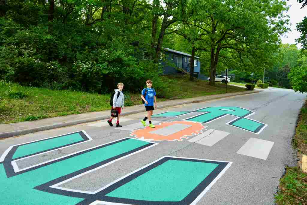 Two individuals jog along a road with large, colorful pedestrian crosswalks painted on the asphalt.