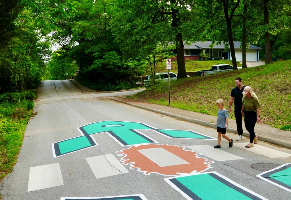 Family walking on a street with a large painted robot figure on the road. Residential house in background.