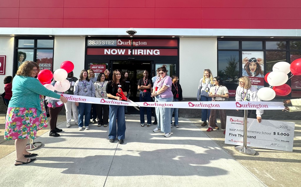 A group of people cutting a ribbon outside a store with a sign that says "Now Hiring."