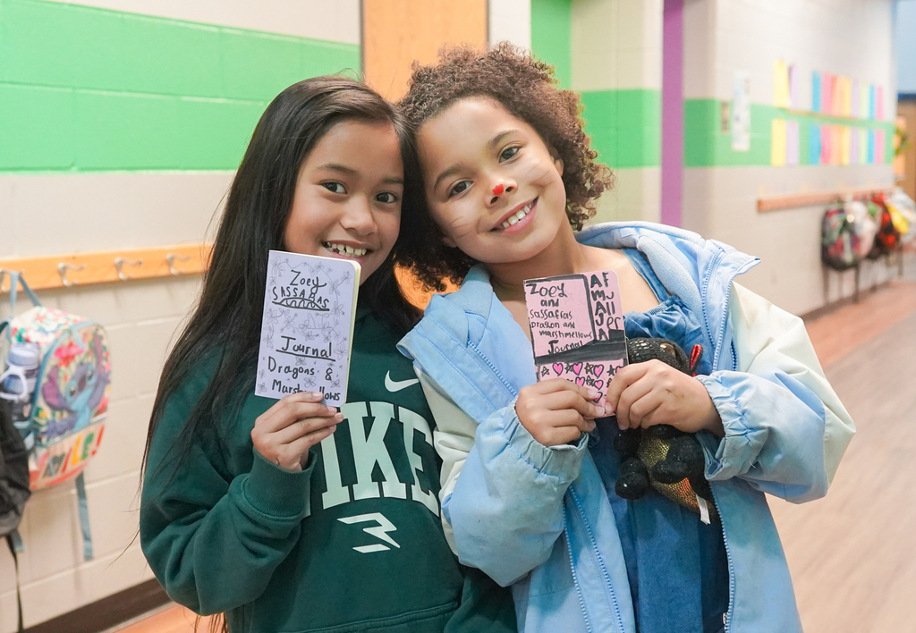 Two girls in a hallway, one holding a red ticket, the other holding a pink ticket, both smiling.