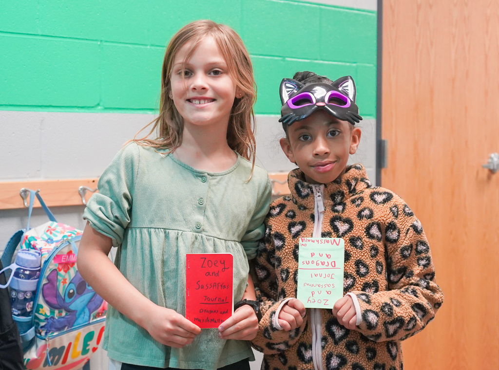 Two children standing inside a room, one holding a red card and the other holding a white card, wearing a cat headband.