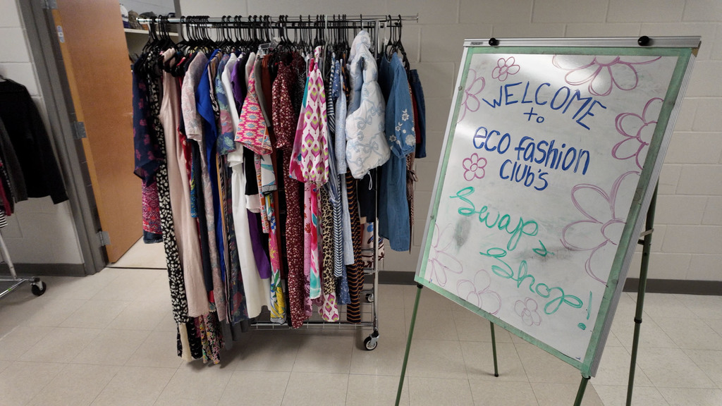 A room with a rack of clothes and a sign saying "Welcome to Eco Fashion Club Swap Shop."
