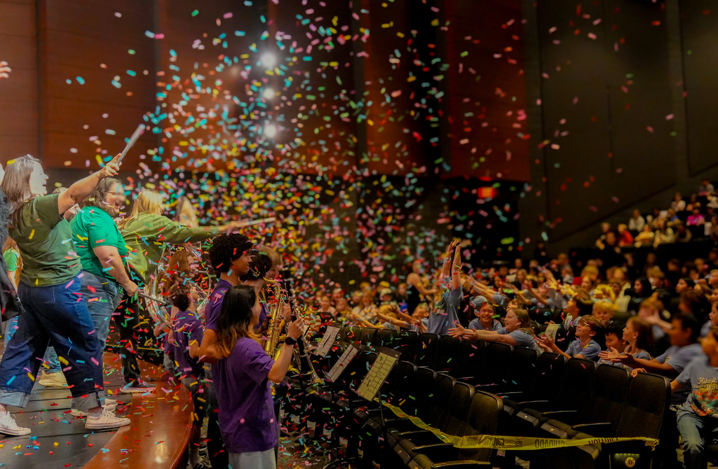 Audience members on a stage and in the audience seats celebrating with colorful confetti in the air.
