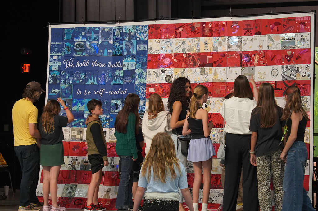 A group of people in front of an American flag made of fabric pieces, engaging with it.