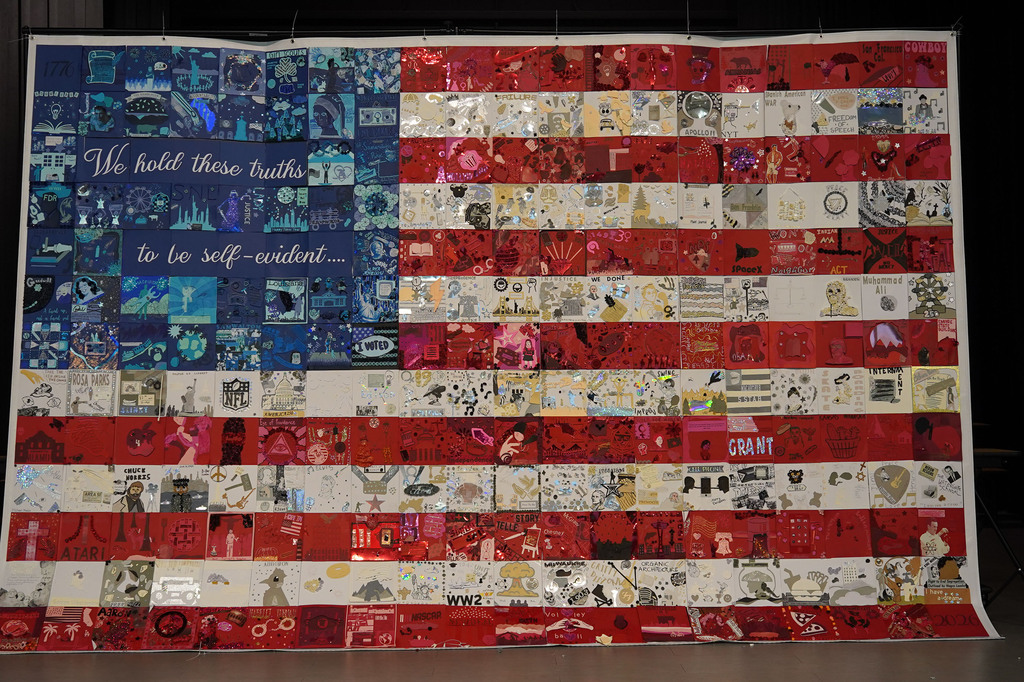 Large quilt with an American flag design, featuring diverse images and a quote in blue lettering at the top.