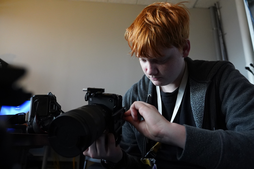 A person with red hair holds a camera and appears to adjust its settings.