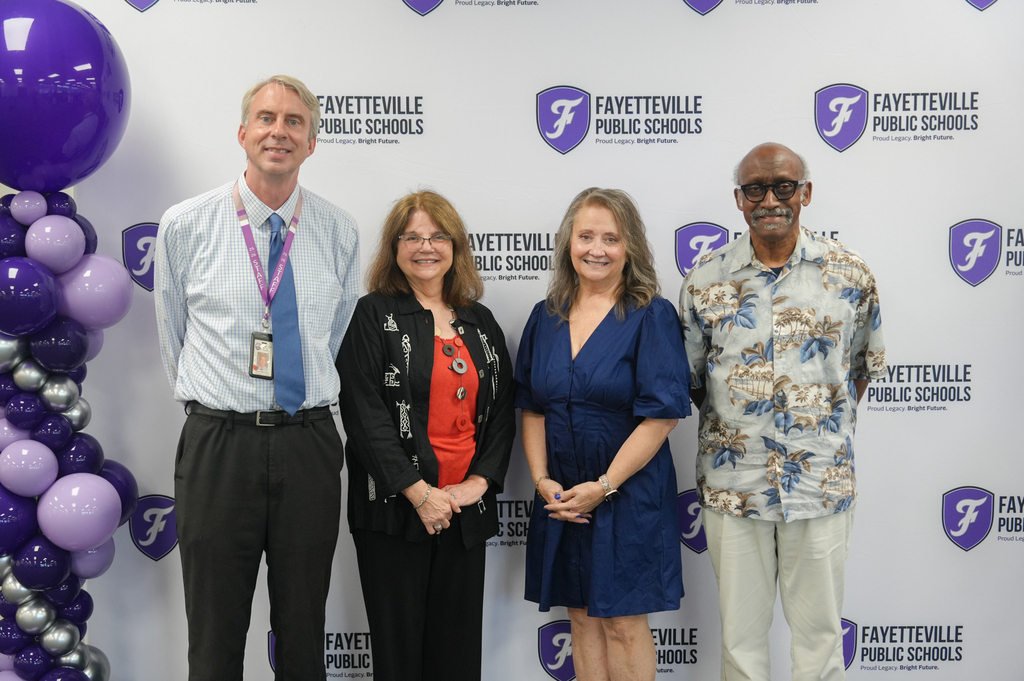 Four adults stand in front of a purple and white balloon backdrop. A logo with the text "Fayetteville Public Schools" is in the background.