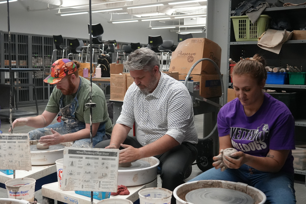 Three people work at tables in a studio, two men with clay and one woman holding clay.