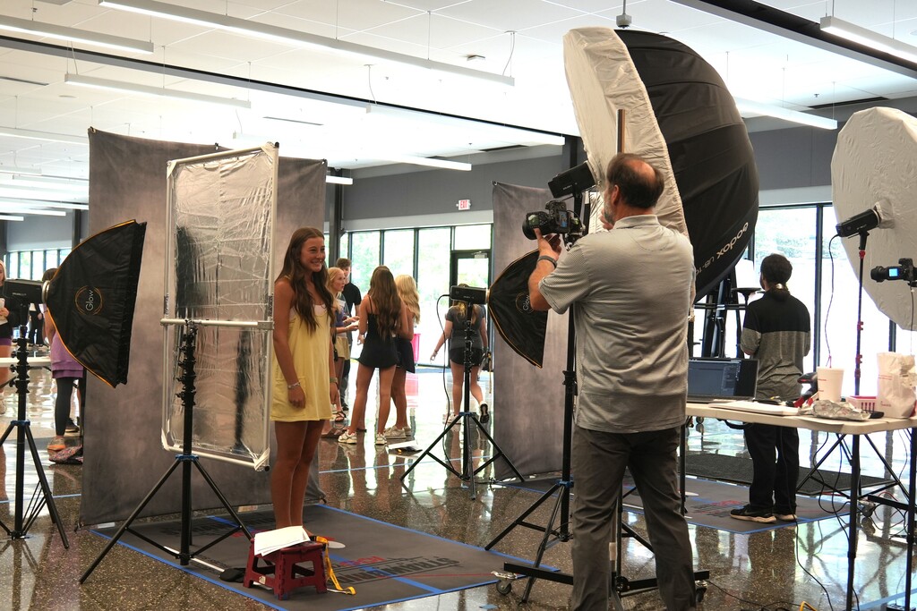 A person is taking photos of a model in a studio. The model stands in front of a backdrop.