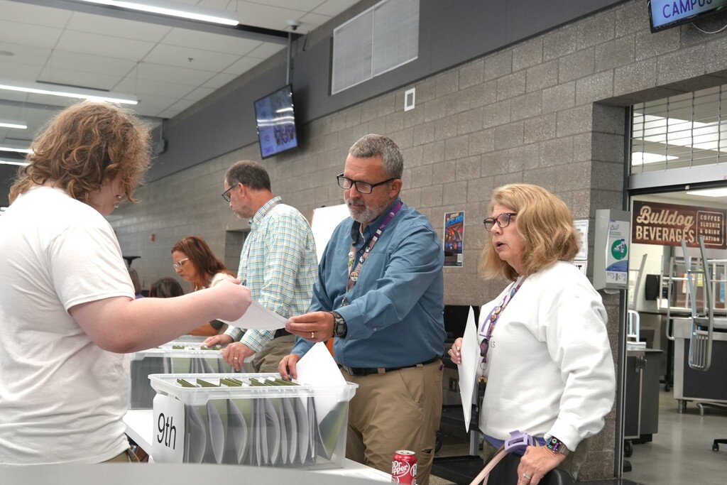 Group of people, two men and two women, standing around a table. One holds papers, another has a box.