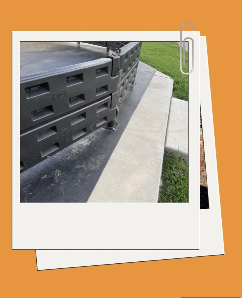 Close-up of stacked gray storage units on a sidewalk with a grassy area on the right.