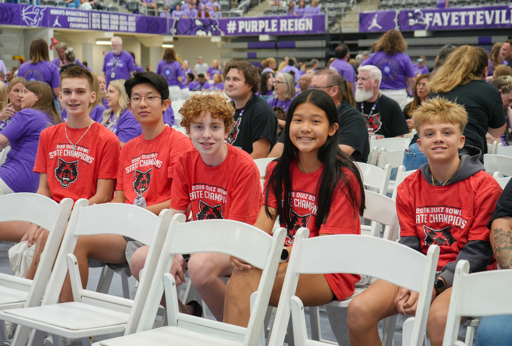 Group of five young people in red t-shirts sit in front row of audience at a sports event.