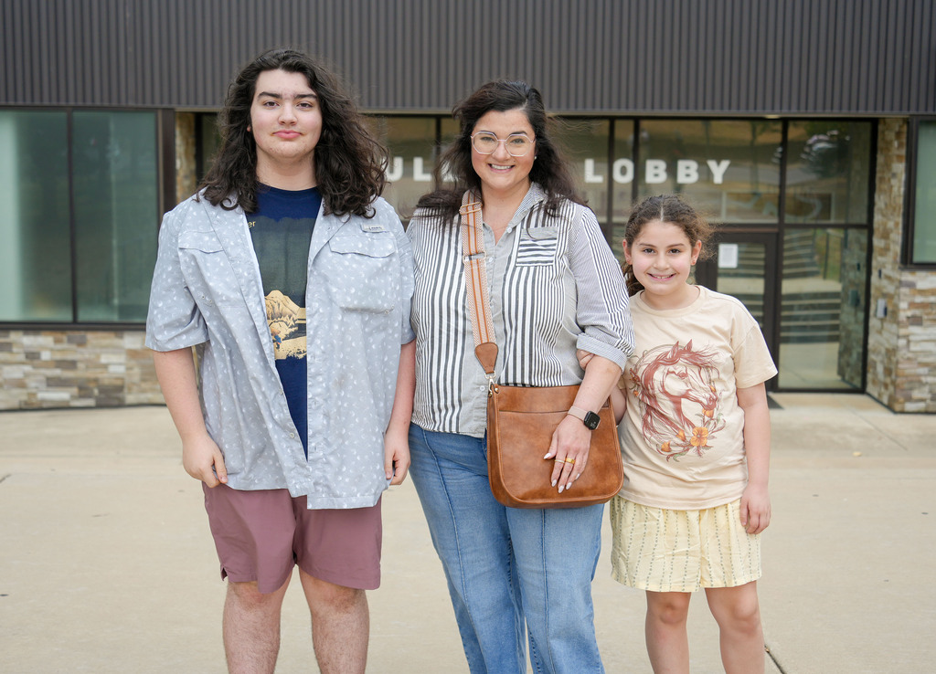 Three people pose for a picture outside a building with a sign reading "JUL LOBBY".