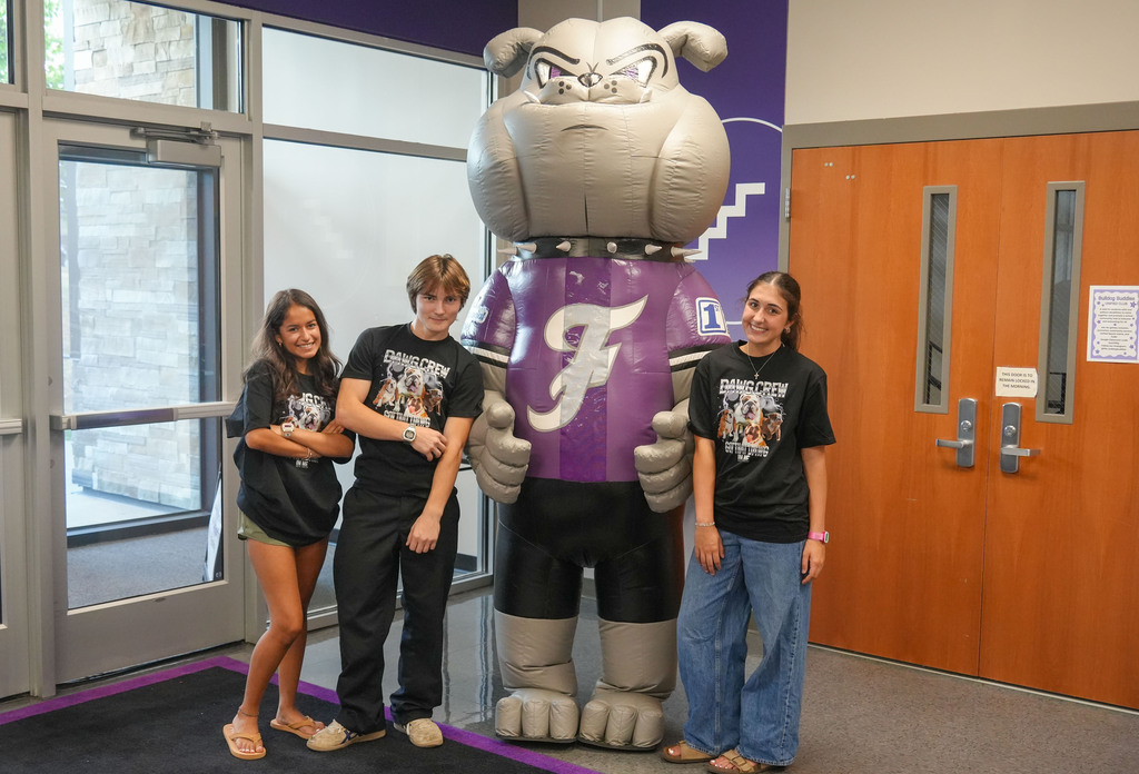 Four kids stand next to a large mascot wearing a purple jersey with the letter F.