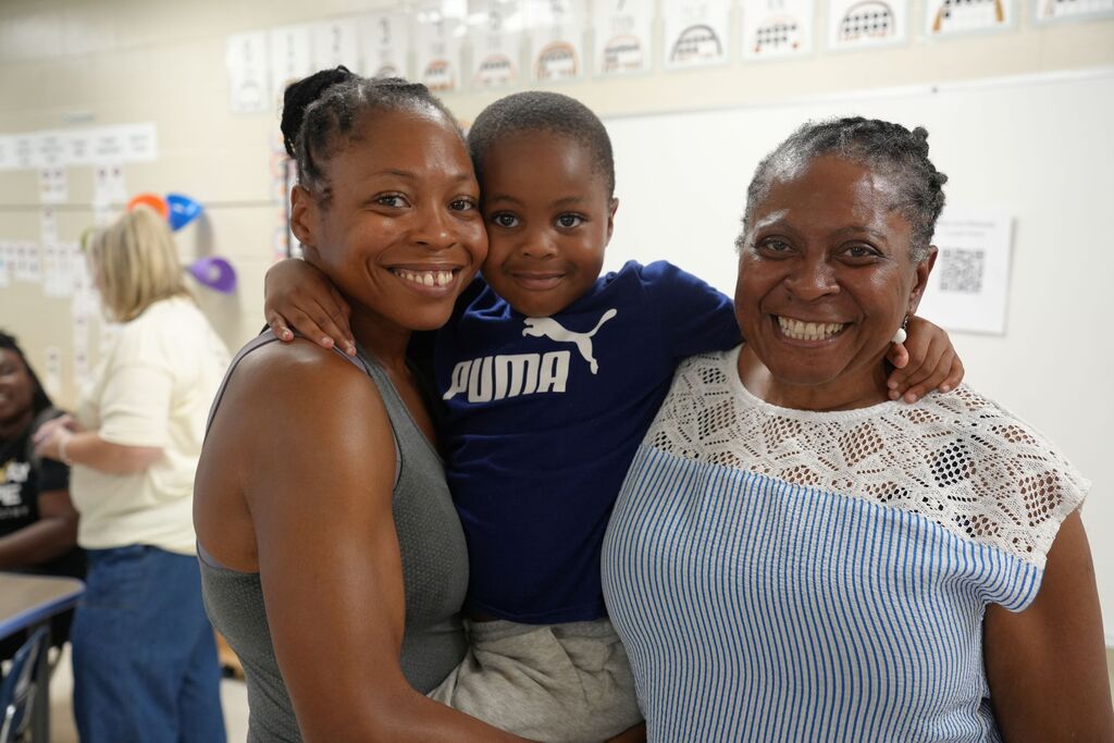 Two women and a boy in a Puma shirt stand together, smiling, with a classroom background.