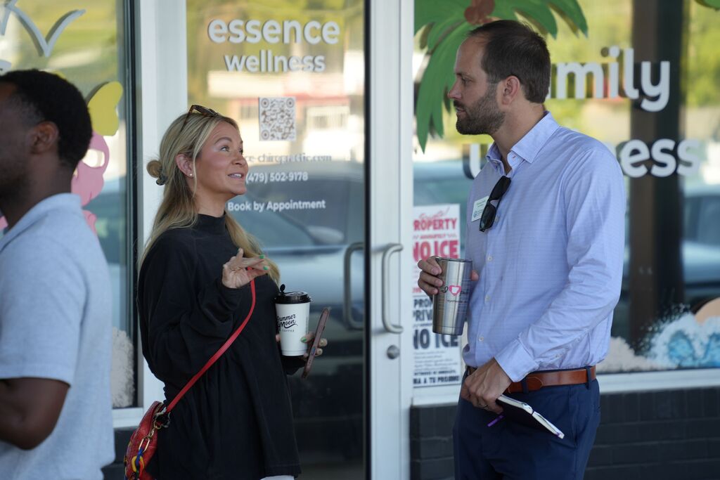 A group of people are standing outside a shop. A woman and a man are looking at each other.