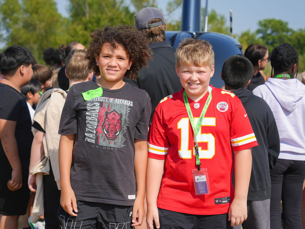 Two boys stand in a crowd, one wearing a black shirt and the other a red football jersey.