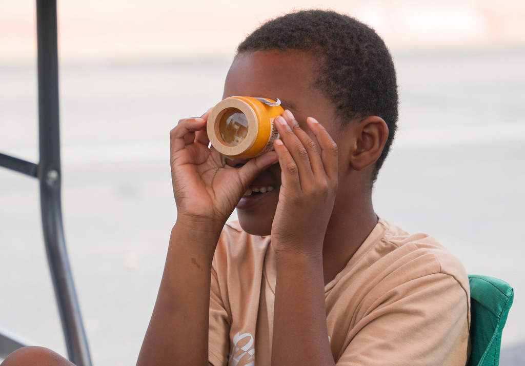 A boy holds a small yellow object to his face, smiling, with a metal structure in the background.