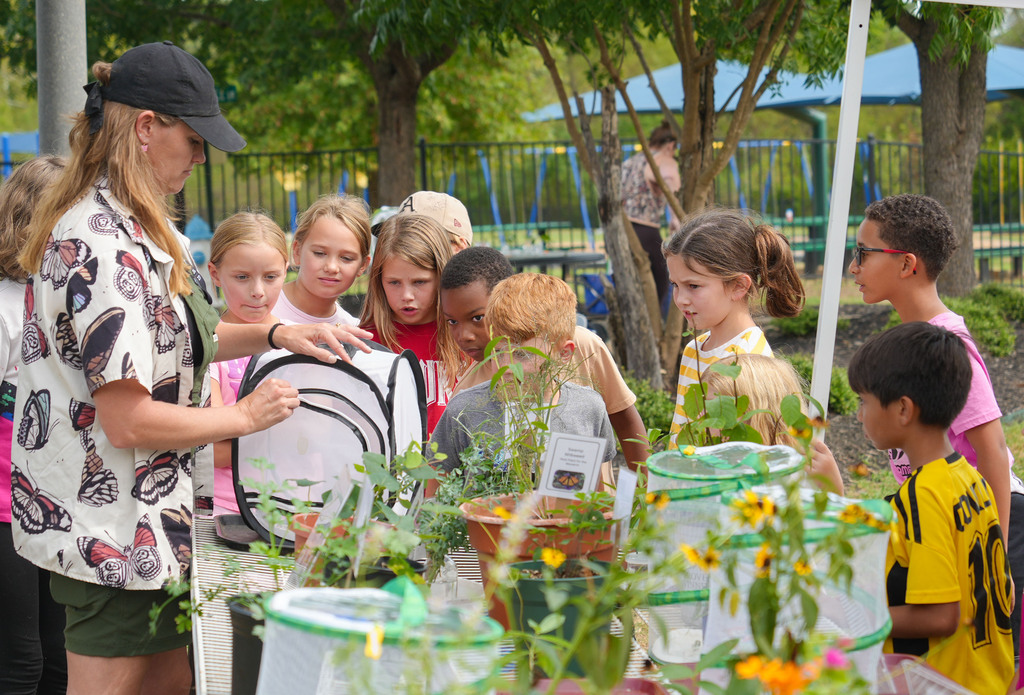 A woman showing plants to children in a park. Some children are wearing hats.