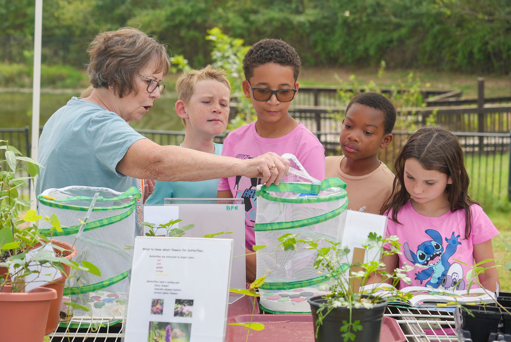 An adult woman teaching children how to plant in a garden with various potted plants.